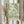 May include: Person holding a framed botanical art print with flowing green foliage pattern on cream background, displayed alongside dried pampas grass stems against soft neutral curtains and window light in minimalist interior setting.