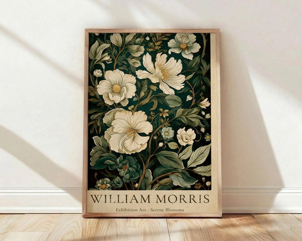 May include: Framed botanical poster with cream flowers and dark green foliage against black background, displayed on light wooden floor against white wall with natural window light creating soft shadows. The wooden frame has natural grain visible, and the artwork shows detailed floral illustrations in vintage style with "WILLIAM MORRIS" and "Exhibition Art - Serene Blossoms" text at bottom.