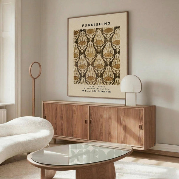 May include: Framed William Morris textile pattern poster with ornate paisley design in brown and cream tones hanging above a mid-century modern walnut credenza. White sculptural chair and glass-top coffee table visible in minimalist living room with cream walls and natural lighting.
