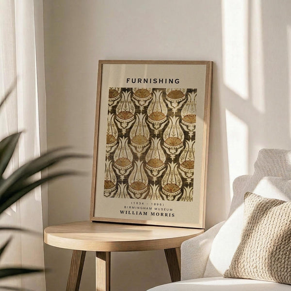 May include: Framed poster with ornate brown and cream paisley pattern displayed on round wooden side table next to beige upholstered chair with knitted throw pillow. Natural sunlight streams across neutral-toned room with plant leaves visible in corner. The vintage-style botanical design features intricate curved motifs in earth tones within thin gold frame.