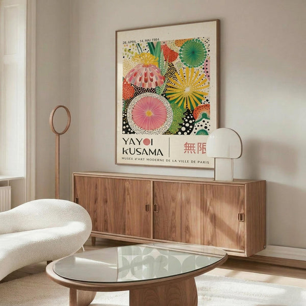 May include: Colorful Yayoi Kusama exhibition poster with vibrant circular patterns in pink, yellow, green, and orange displayed above a mid-century modern wooden credenza. The artwork features radiating dots and geometric designs in a contemporary living room with white curved chair, glass coffee table, and minimalist decor.
