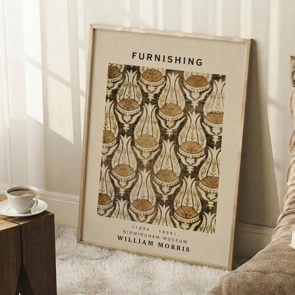 May include: Framed vintage-style poster with "FURNISHING" text and ornate brown and cream decorative pattern featuring stylized vessels and flourishes, attributed to William Morris (1834-1896) Birmingham Museum. Light wood frame leaning against white paneled wall beside wooden side table with white coffee cup, cream textured rug, and soft beige throw blanket visible.