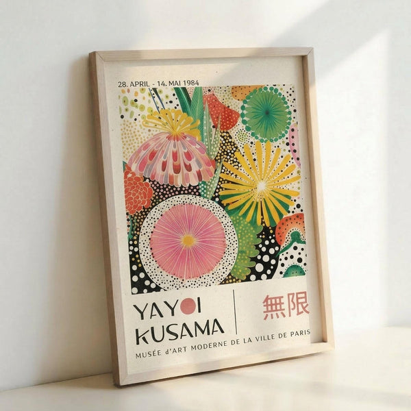 Colorful exhibition poster featuring vibrant circular and radiating patterns in pink, yellow, green, and orange with polka dot backgrounds. The artwork displays geometric flowers and sunburst designs against black dotted areas. Text shows dates "28. APRIL - 14. MAI 1984" at top, "YAYOI KUSAMA" in large letters, Japanese characters, and "MUSÉE d'ART MODERNE DE LA VILLE DE PARIS" at bottom. The poster is displayed in a light wooden frame leaning against a white wall.