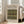 May include: Framed poster displaying William Morris woven fabric pattern with tulips and roses in olive green, burgundy red, and golden yellow tones against cream background. Light wood frame leans against white wall next to beige upholstered sofa in bright, modern living room with large windows and natural lighting.