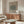 May include: Beige and sage green vintage-style botanical poster displayed above wooden sideboard in minimalist living room with houndstooth chair, glass coffee table, and modern white mushroom lamp. Natural lighting creates warm shadows on cream walls.
