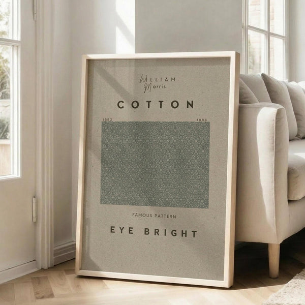 May include: Framed poster with beige background featuring William Morris Cotton pattern from 1882-1883. Green textured square pattern sample labeled "Eye Bright" displayed in light wood frame, leaning against white wall next to beige upholstered chair in bright, sunlit room with hardwood floors.