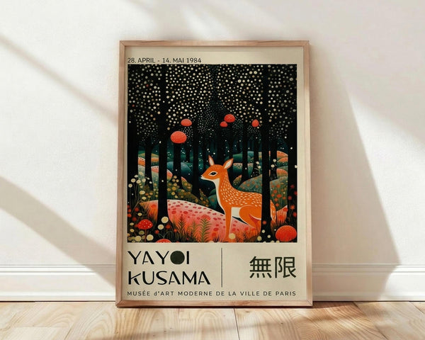 May include: Framed exhibition poster featuring a spotted deer in an enchanted forest scene with red mushrooms, white dots falling like snow against a black starry sky, and colorful foliage. The artwork shows Japanese text and museum details below the whimsical illustration. The light wood frame leans against a white wall on wooden flooring with soft natural lighting creating diagonal shadows.