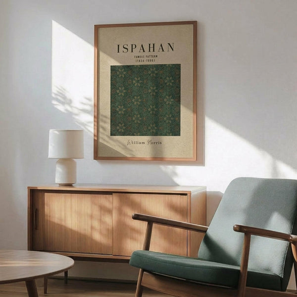 May include: Framed poster featuring William Morris's Ispahan pattern in green tones displayed above a wooden sideboard with table lamp. Mid-century modern living room setting with sage green upholstered chair, round coffee table, and natural sunlight casting shadows on white walls.