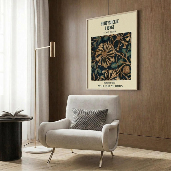 May include: Beige armchair with geometric pillow beneath framed botanical poster on wood-paneled wall. Poster shows dark blue background with golden honeysuckle flowers and green leaves in decorative pattern. Modern reading corner with brass floor lamp, black side table with open book, and light wooden flooring.