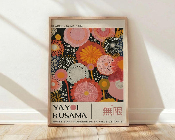 May include: Framed poster with colorful circular and radial patterns in pink, orange, yellow, and black with white dots, displayed against white wall on light wood floor. Shows "YAYOI KUSAMA" text and "28. APRIL - 14. MAI 1984" exhibition dates, with "MUSÉE d'ART MODERNE DE LA VILLE DE PARIS" at bottom. Natural wood frame, soft lighting creates diagonal shadows across white wall.