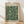 May include: Framed botanical print with dark green background featuring cream-colored flowers and flowing foliage in vintage Arts and Crafts style. Natural wood frame leans against white wall on light wooden floor with soft shadows from window light. Quote text appears at bottom of artwork.