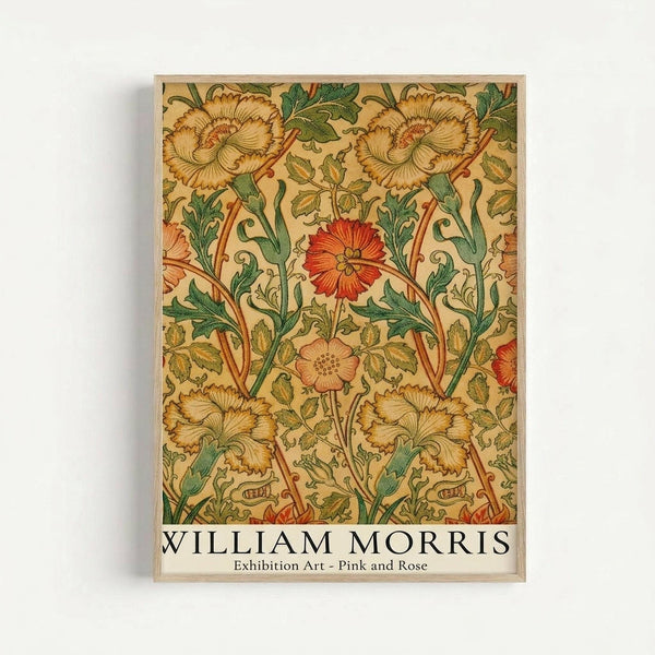 Framed vintage botanical wallpaper design featuring ornate floral pattern with large golden carnations, bright red flowers, and pink blooms connected by flowing green stems and leaves on cream background. Arts and Crafts movement style with intricate detail and rich earth tones, displayed in light wood frame against white wall.