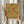 May include: Person in cream sweater holding framed botanical art print featuring William Morris floral pattern with large blooms in yellow, orange, and red tones with green foliage on cream background. White wooden frame, dried pampas grass visible to left, soft natural lighting against neutral curtained background.