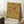 May include: Framed botanical poster with William Morris floral pattern featuring golden carnations, red poppy flowers, and green foliage on cream background, leaning against white wall beside wooden side table with white coffee cup and saucer, on textured white rug with beige throw blanket visible.