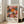 May include: Framed vintage exhibition poster featuring colorful circular patterns and radiating designs in pink, orange, black, and white. Shows dates "28. APRIL - 14. MAI 1984" and "YAYOI KUSAMA MUSEE d'ART MODERNE DE LA VILLE DE PARIS" text. Light wood frame leans against white wall next to beige upholstered sofa in bright room with large windows.