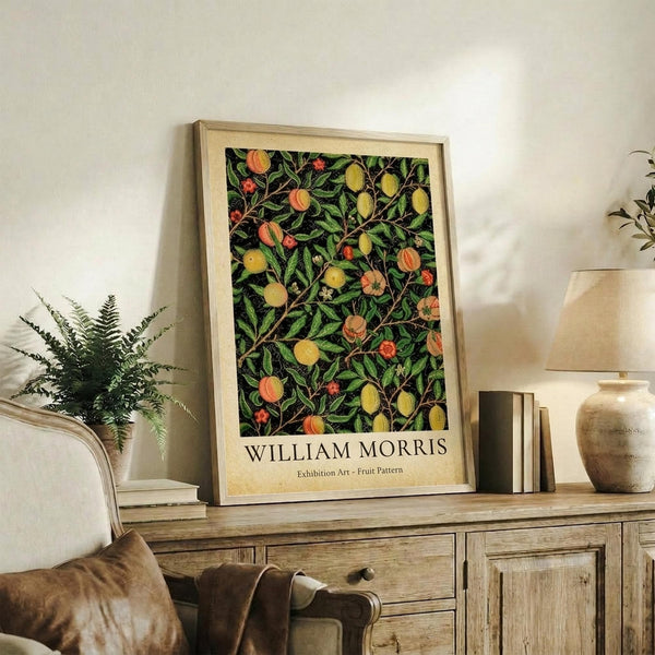 May include: Framed botanical art print featuring colorful fruit and flower pattern with green leaves, yellow lemons, orange peaches, and red berries on dark background. Light wood frame displayed on rustic wooden sideboard alongside books, ceramic vase, and fern plant in neutral-toned living room setting.