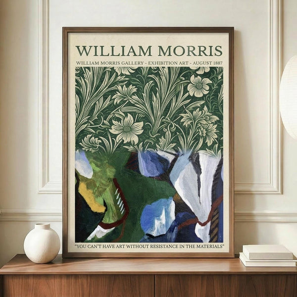 May include: Framed poster with William Morris Gallery exhibition text at top, featuring green botanical pattern with cream flowers and leaves in upper half, abstract painted elements in blues, greens, and whites below, quote at bottom. Wooden frame on light wood credenza beside white ceramic vase and stacked books against cream wainscoted wall.