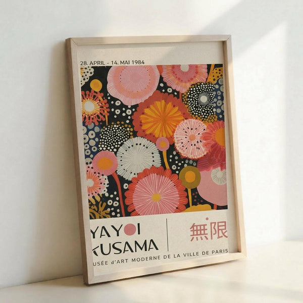 Colorful exhibition poster featuring vibrant circular and radial patterns in pink, orange, yellow, and black with white dots scattered throughout. Text shows dates "28. APRIL - 14. MAI 1984" at top and "YAYOI KUSAMA" with Japanese characters and "MUSEE D'ART MODERNE DE LA VILLE DE PARIS" at bottom. The artwork displays overlapping floral and geometric shapes creating a dynamic, psychedelic composition. Poster is displayed in a light wooden frame leaning against a white wall