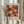 May include: Person holding framed poster featuring colorful abstract circular patterns in pink, orange, yellow and black with dotted details. Light wood frame against neutral curtained background with dried pampas grass visible. Exhibition poster shows dates 28 April - 14 Mai 1984 and Musée d'Art Moderne de la Ville de Paris text below vibrant radiating botanical-inspired design.