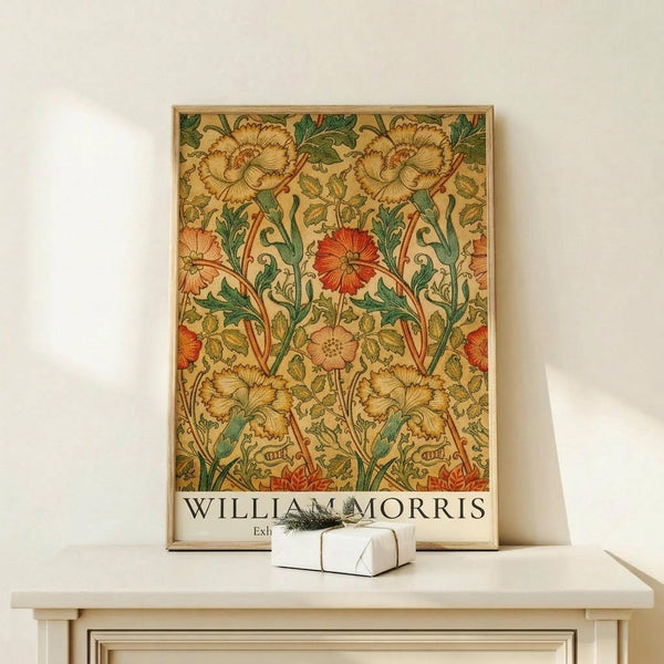 May include: Framed botanical poster with ornate floral pattern featuring large blooming flowers in golden yellow and coral red tones with green foliage on cream background, displayed on light wood console table next to small white gift box with dried sprig, against neutral wall in modern interior setting.