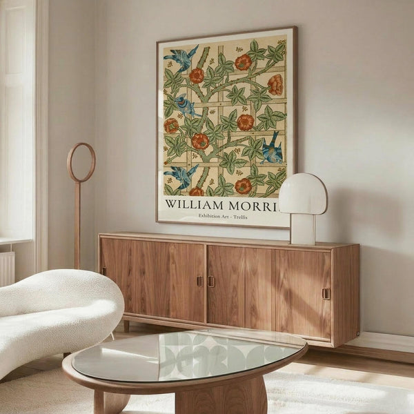 May include: Framed botanical poster with blue birds, orange flowers, and green foliage on cream background displayed above walnut wood credenza in neutral living room. White curved chair and glass coffee table visible in foreground with natural sunlight casting shadows across scene.