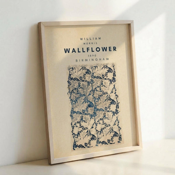 May include: Framed vintage botanical wallpaper design print in cream and blue tones, featuring intricate floral patterns with curved stems and delicate blooms. The artwork displays in a light wood frame, leaning against a white wall. The design shows ornate Victorian-era decorative motifs with flowing organic shapes and detailed botanical elements in muted blue-green hues on an off-white background.