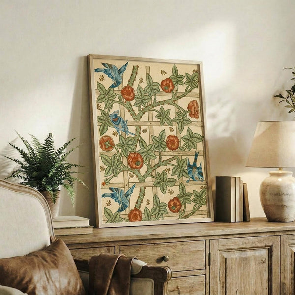 May include: Framed botanical print featuring blue birds, red flowers, and green foliage in a trellis pattern displayed on a rustic wooden sideboard beside a fern plant, books, and ceramic vase in a neutral-toned living room with beige upholstered furniture and warm natural lighting.