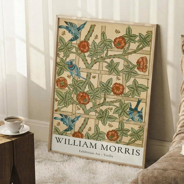 May include: Framed botanical poster print featuring blue birds among orange flowers and green foliage in a decorative trellis pattern, displayed against white paneled walls near a wooden side table with coffee cup and cozy throw blanket on carpeted floor.