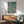 May include: Framed botanical art print with blue background featuring colorful fruits, flowers, and green leaves in William Morris style, displayed above wooden sideboard with table lamp in modern living room setting with mid-century green armchair and round coffee table