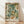 May include: A framed botanical art print leaning against a white textured wall on light wood flooring. The artwork features an intricate floral pattern with large cream and white blooms, sage green foliage, and small orange berries in William Morris's distinctive decorative style. Natural window light casts soft diagonal shadows across the scene. The print is housed in a simple light wood frame.