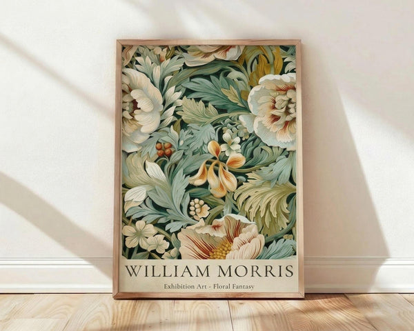 May include: A framed botanical art print leaning against a white textured wall on light wood flooring. The artwork features an intricate floral pattern with large cream and white blooms, sage green foliage, and small orange berries in William Morris's distinctive decorative style. Natural window light casts soft diagonal shadows across the scene. The print is housed in a simple light wood frame.