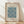 May include: Framed art print featuring William Morris's blue Marigold pattern with intricate floral and leaf designs on cream background, displayed in light wood frame against white wall on wooden floor with soft natural lighting creating diagonal shadows.