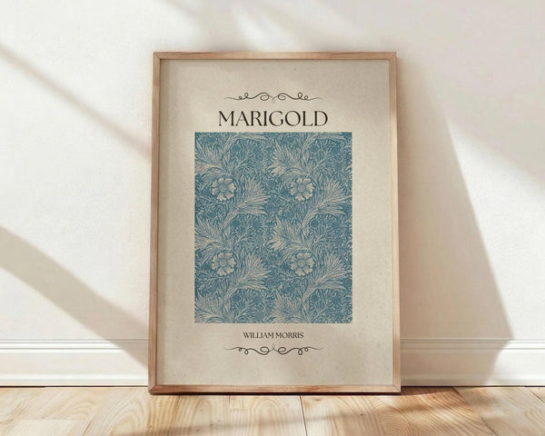 May include: Framed art print featuring William Morris's blue Marigold pattern with intricate floral and leaf designs on cream background, displayed in light wood frame against white wall on wooden floor with soft natural lighting creating diagonal shadows.