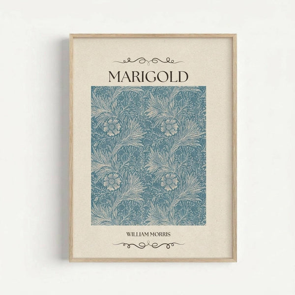 A framed botanical art print featuring William Morris's Marigold pattern in dusty blue tones. The decorative floral design shows interwoven marigold flowers and flowing foliage in an intricate repeating pattern. The artwork is displayed in a light wood frame with cream matting against a white wall, with elegant serif typography above and below the pattern sample.