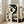 May include: Large framed abstract art print featuring a stylized woman's profile in black, cream, and gray tones with geometric shapes and circles. The artwork leans against a white wall next to a beige upholstered chair in a bright, minimalist living room with large windows and natural lighting.