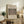 May include: Framed botanical poster with intricate honeysuckle pattern in muted greens and pinks, displayed on rustic wooden sideboard alongside fern plant, stacked books, and ceramic vase in warm, neutral-toned living room setting with upholstered furniture and soft natural lighting.