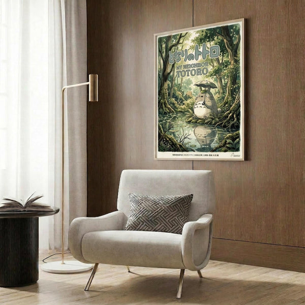 May include: Framed Studio Ghibli My Neighbor Totoro movie poster hanging on wood-paneled wall above beige upholstered armchair with geometric patterned pillow. Poster shows Totoro characters in lush green forest scene with Japanese text. Modern reading nook with brass floor lamp, side table with open book, and natural lighting from window with curtains.
