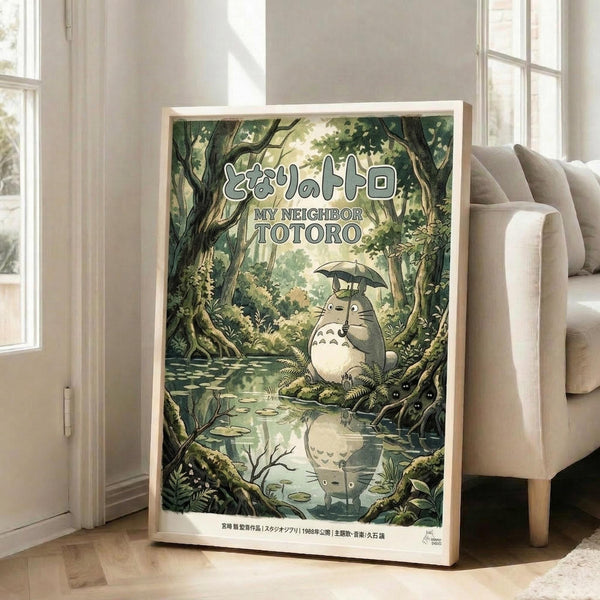 May include: Framed poster displaying animated forest scene with large gray creature holding umbrella, sitting by reflective water surrounded by lush green trees and foliage. Japanese text appears at top with English translation below. Light wooden frame leans against white wall beside beige upholstered chair in bright, naturally-lit room with hardwood floors.