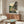 May include: Framed Studio Ghibli anime poster showing Totoro and a small girl sitting on a bench outside a traditional Japanese house with mountains in the background. Displayed above a mid-century modern walnut credenza in a minimalist living room with cream walls, white upholstered chair, glass coffee table, and warm natural lighting.