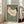 May include: Large framed vintage Japanese woodblock print of a walking hen displayed in a bright living room. The artwork features a cream-colored chicken with black tail feathers and red comb against sage green background, housed in natural wood frame. Print leans against white wall next to beige upholstered chair with windows showing natural light.