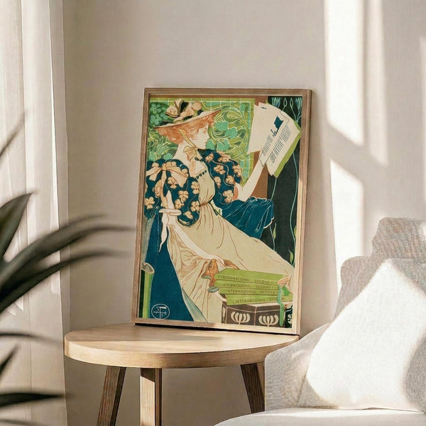 May include: Art Nouveau poster print in wooden frame displayed on round wooden side table next to beige upholstered chair. Artwork features elegant woman with flowing auburn hair in white dress against green background with ornate decorative elements. Soft natural lighting creates shadows on neutral wall. Plant leaves visible in corner of minimalist interior setting.