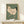 May include: Vintage Japanese woodblock print of a white hen with black tail feathers and red comb on sage green background, displayed in thin wooden frame on light wood shelf next to small white wrapped gift with natural twine and dried sprig accent against cream wall