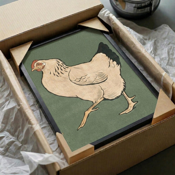 Vintage Japanese woodblock print of a plump cream-colored hen with black tail feathers and red comb, walking on orange legs against a muted green background. The artwork is displayed in a black frame, partially unwrapped from brown cardboard packaging with white tissue paper visible around the edges.