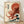 May include: Framed Japanese-style woodblock print artwork featuring a large red octopus with curling tentacles emerging from stylized blue ocean waves with white foam. The vintage-inspired poster has Japanese text characters on cream-colored aged paper background with red circular sun element. Displayed in light wood frame leaning against white wall on wooden floor with soft natural lighting and shadows.