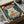 May include: Framed poster print in wooden frame showing white cat with golden eyes eating from bowl of ramen noodles with eggs and meat, featuring Japanese text characters in red boxes on teal background, vintage-style illustration, displayed in shipping box with protective tissue paper wrapping