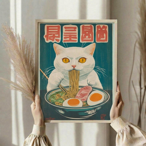 May include: Hands holding a framed poster featuring a white cat with yellow eyes eating noodles from a ramen bowl, with red Japanese characters above on a teal background. The wooden-framed artwork is displayed against white curtains, with dried wheat stems visible to the left. The vintage-style illustration shows the cat using chopsticks with eggs, meat, and vegetables in the bowl.