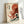 May include: Framed poster print leaning against white wall showing Japanese woodblock-style artwork featuring large red octopus with tentacles emerging from ocean waves. Design combines traditional blue and white wave patterns with bold red octopus against cream background, includes Japanese text and red sun. Light wood frame, soft natural lighting creates subtle shadows on wall.