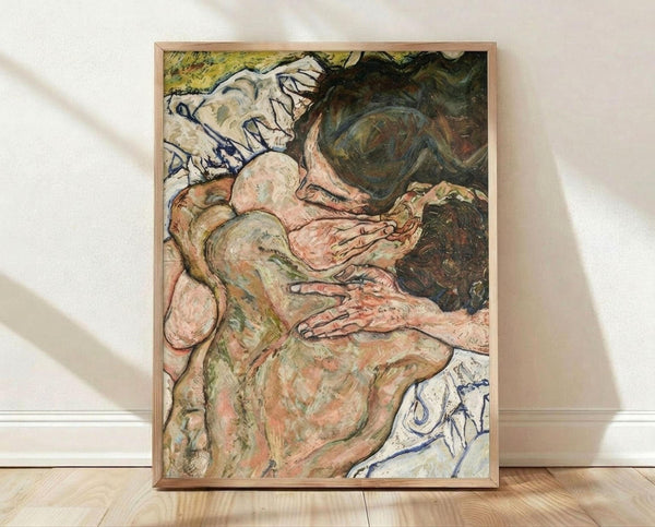 May include: Framed art print leaning against white wall on light wood floor. The artwork shows two embracing nude figures rendered in expressive brushstrokes using muted greens, pinks, and whites with dark blue linear details. The intimate composition features flowing, organic forms typical of early 20th century expressionist style. Natural light casts soft shadows on the textured white wall behind the thin wooden frame.