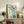 May include: Framed Asian-style painting featuring five tall blue cranes with brown heads arranged in a line, accompanied by black Chinese calligraphy on white background. Light wood frame displayed on rustic wooden credenza alongside fern plant, ceramic vase, and books in neutral-toned living room setting.