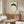 May include: Japanese ink brush painting of a minimalist black frog in a circular pose against cream background, displayed in thin brown frame above mid-century modern walnut credenza. Room features white curved chair, brass floor lamp, oval glass coffee table with blue accent, and white walls with natural lighting.
